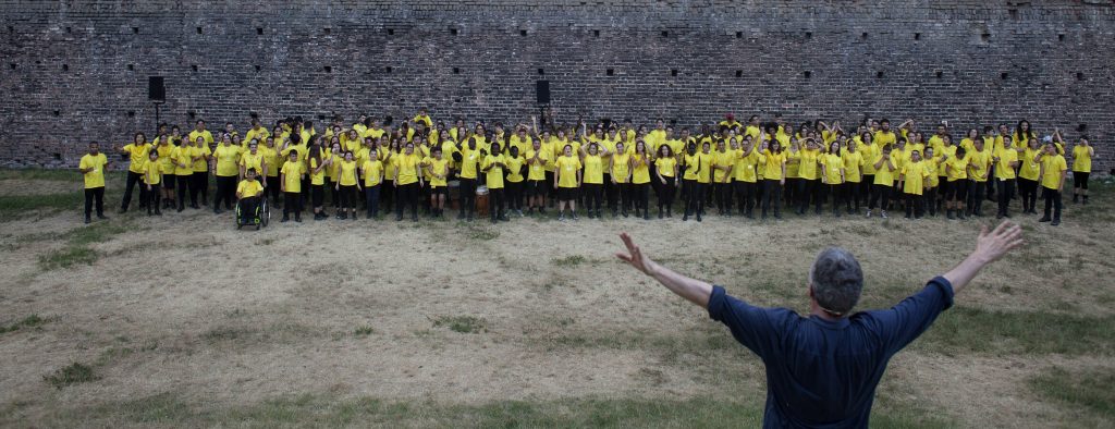 Marco Martinelli di schiena dirige gruppo di bambini con tshirt gialla
