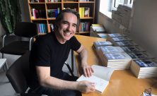 Matteo Bussola sorridente alla scrivania mentre firma i suoi libri