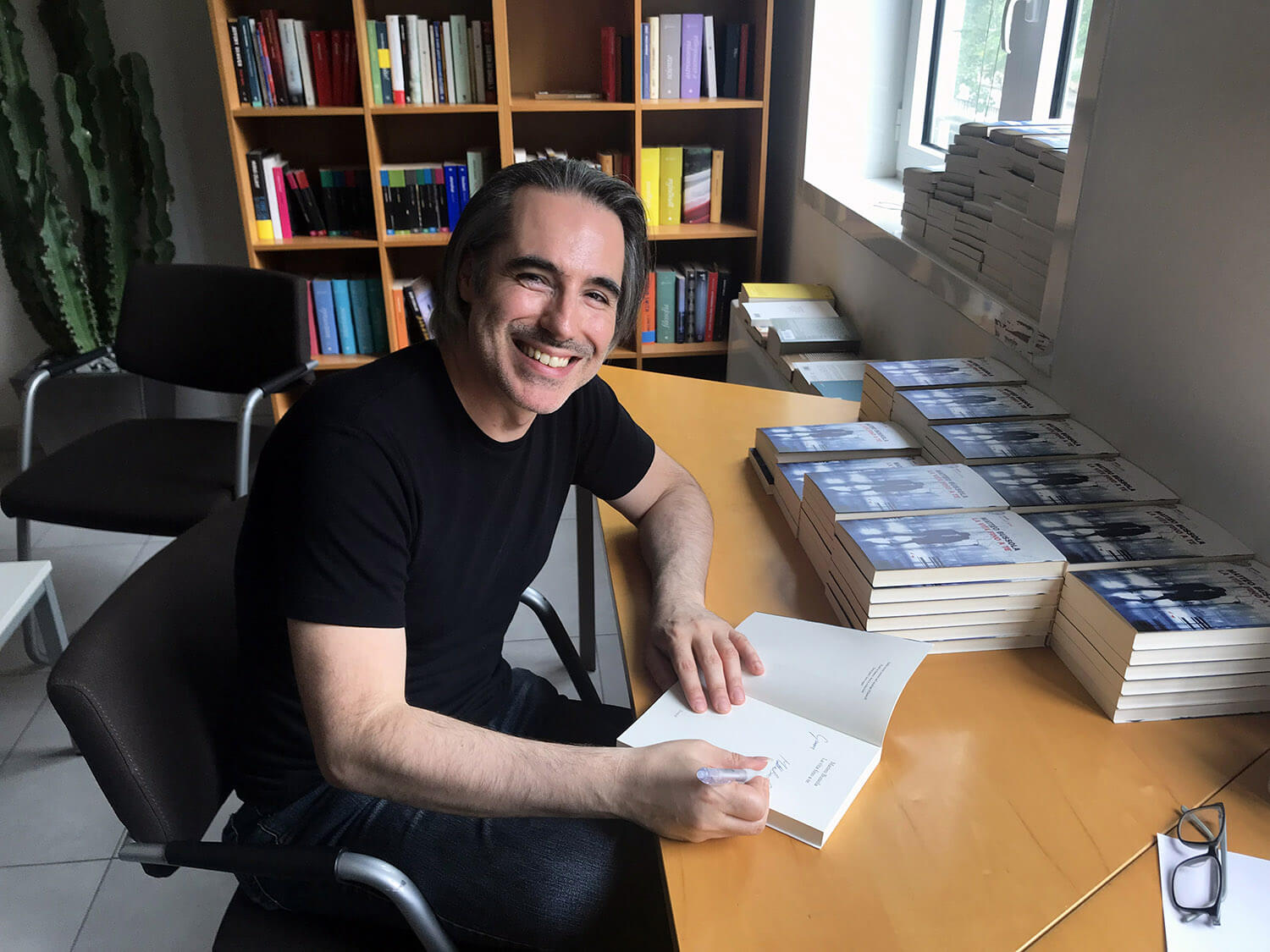 Matteo Bussola sorridente alla scrivania mentre firma i suoi libri