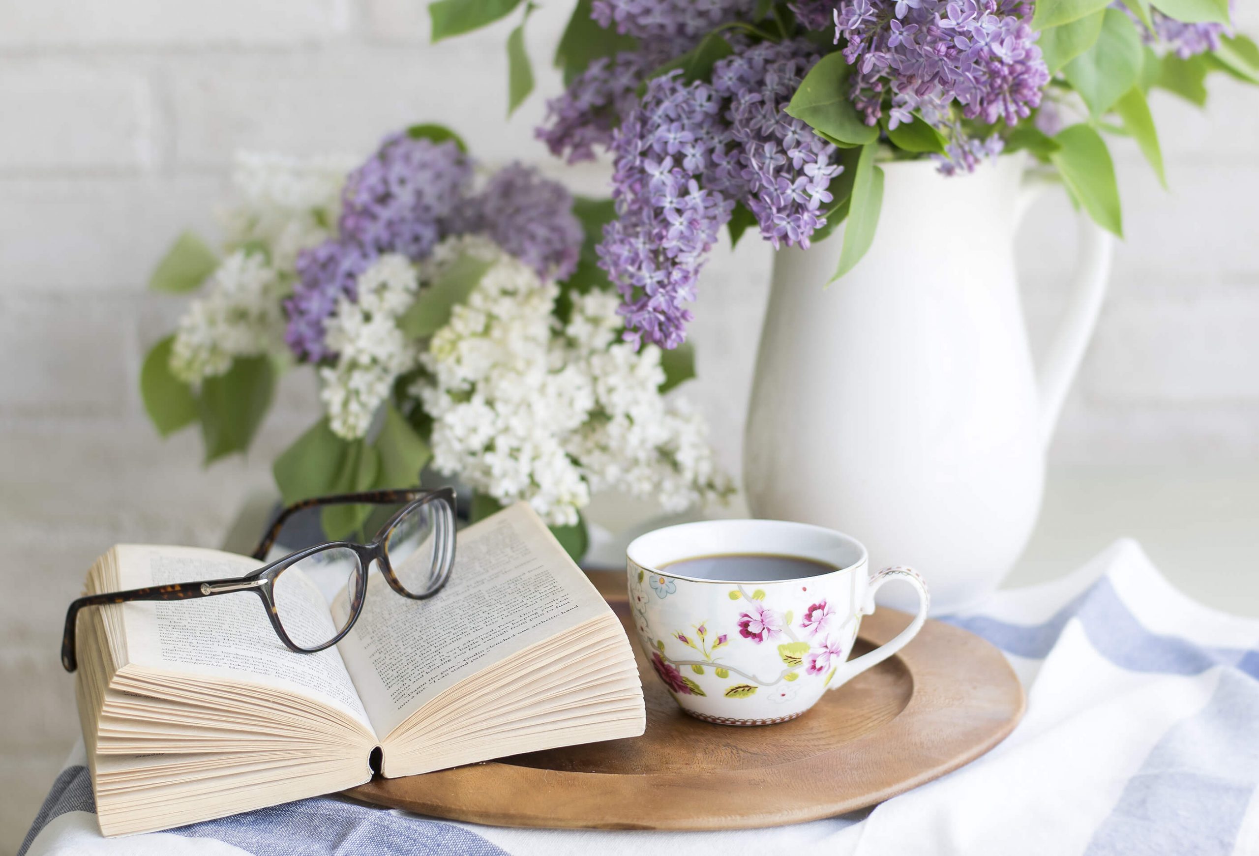 Libro aperto con occhiali appoggiati vicino ad una tazzina da caffè e sullo sfondo dei fiori