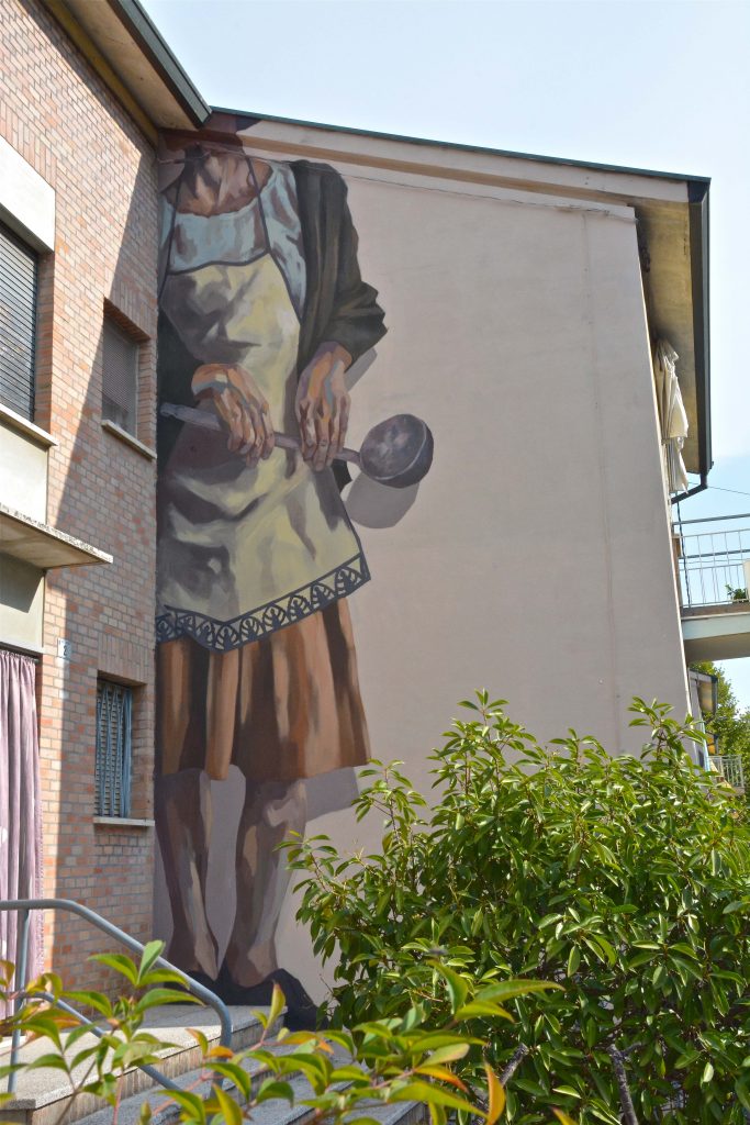 Murale sul lato di un'abitazione che rappresenta un'adora senza testa con un mestolo in mano