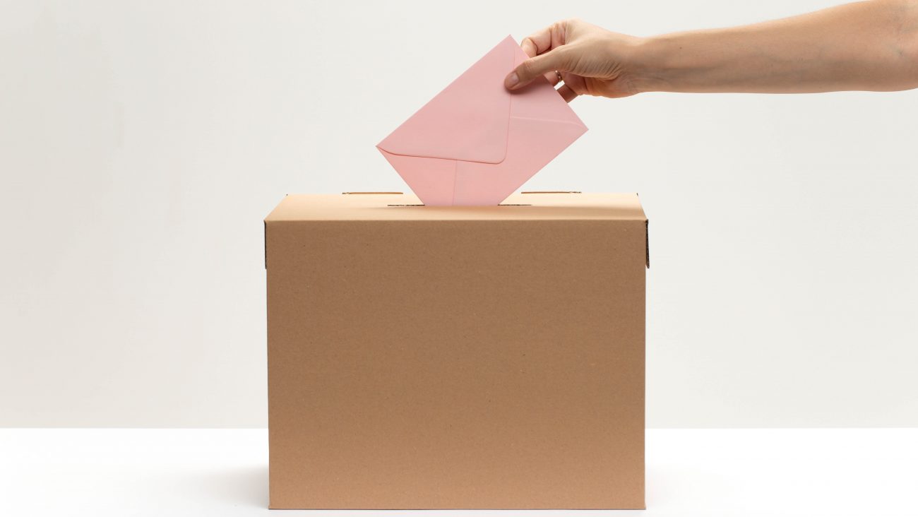 hand-puts-pink-envelope-into-vote-box